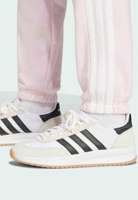 Hvit og svart sporty sko med gummisåle, laget av semsket skinn og lær, med svarte striper og snøring, kombinert med rosa joggebukser.