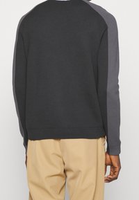 Czarny sweter z dekoltem typu pulower z ciemnoszarymi akcentami na ramionach, ściągacze przy mankietach i u dołu, gładka tekstura, prosty design oraz luźny krój.