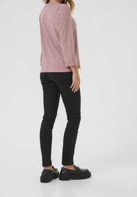 Top rosa chiaro in pizzo con maniche a tre quarti, abbinato a jeans skinny neri e mocassini neri con plateau, visto da dietro.