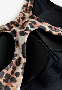 Vêtement de sport noir avec une bande à motif léopard. Présente des motifs texturés et des détails de couture. Construction soignée et mélange de tissus visible.