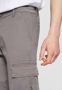 Szürke cargo nadrág, texturált felülettel, amely több zsebet, slim fit szabást és gombos zárást tartalmaz a deréknál.