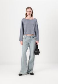 Top cinza cropped de mangas longas, jeans flare azuis desbotados e bolsa preta. O top tem bordas desfiadas; os jeans têm bolsos e costuras visíveis.