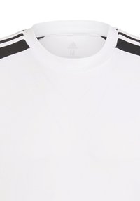 Camiseta atlética blanca con cuello redondo, hecha de una tela suave; presenta tres franjas negras en los hombros y un logo de Adidas.