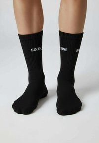 Chaussettes noires à texture côtelée, avec le texte blanc « SIXTH JUNE » de chaque côté, couvrant la partie inférieure de la jambe, avec une coupe mi-mollet.