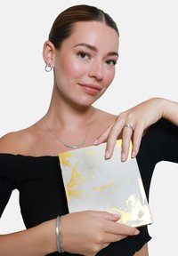 Glanzend gouden accentjournal vastgehouden door een persoon die zilveren sieraden draagt. Het journal heeft een gemarmerd wit en gouden ontwerp met ingebosselde tekst.