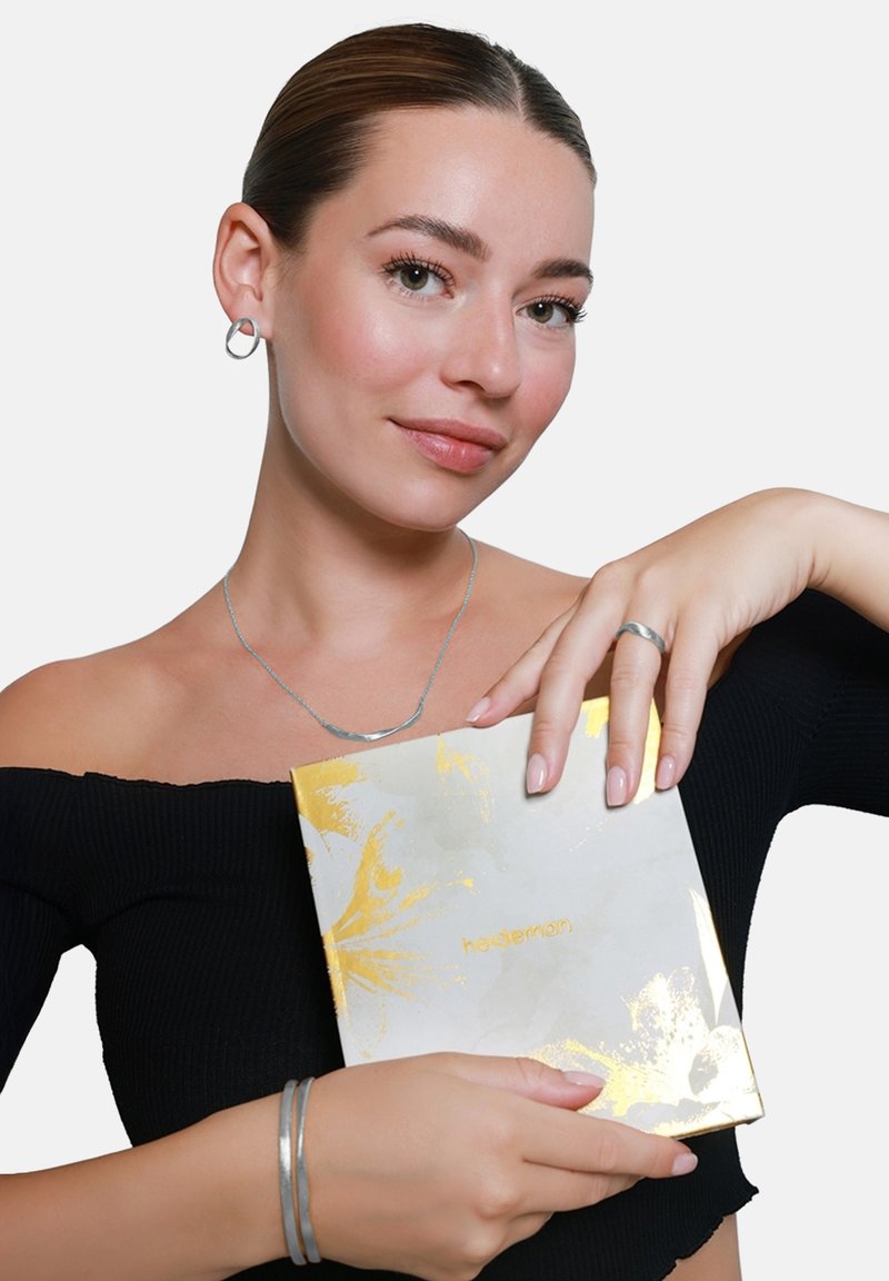 Glanzend gouden accentjournal vastgehouden door een persoon die zilveren sieraden draagt. Het journal heeft een gemarmerd wit en gouden ontwerp met ingebosselde tekst.