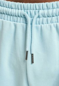 Light blue sweatpants featuring an elastic waistband with gathered texture, drawstrings, and metal aglets for adjustments.