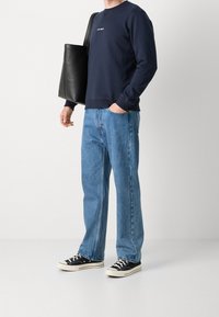 Sweatshirt blu navy con collo a giro, jeans dritti blu chiaro, sneakers in tela nere e una borsa tote in pelle nera.