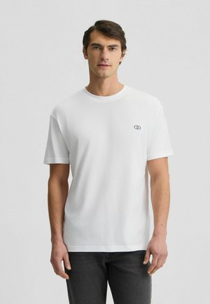 T-shirt bianco in cotone a maniche corte con scollo rotondo e un piccolo logo blu sul lato sinistro del petto. Ideale per un look informale.