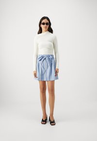 Top bianco a maniche lunghe, gonna plissettata a righe blu chiaro con cintura in vita e scarpe con tacco aperte nere. Design semplice e pulito.