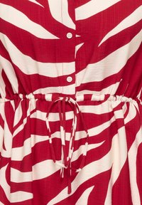 Robe à rayures rouges et blanches avec fermeture à boutons et ceinture ajustable à la taille, présentant un motif audacieux et abstrait.