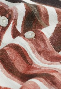 Gros plan d’un tissu rayé marron, beige et blanc avec deux boutons ronds couleur crème cousus sur un tissu texturé.