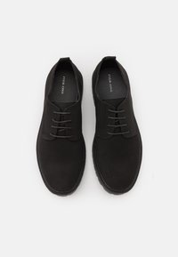 Chaussures en suede noir avec une finition lisse, un bout arrondi et un design à laçage à cinq œillets. La doublure intérieure présente le texte de la marque "PIER ONE."