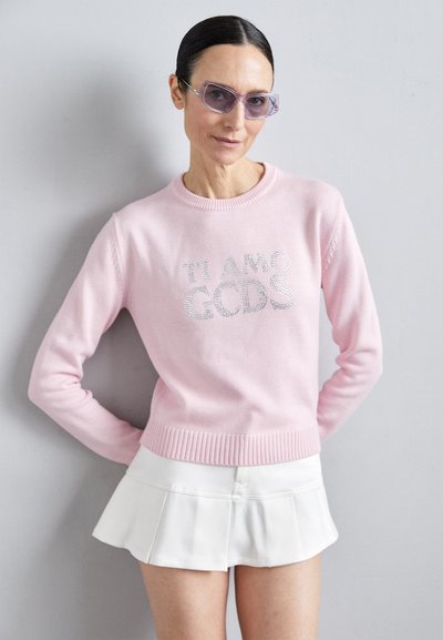 Pink knitted sweater with "TI AMO GCDS" in rhinestones, paired with a white pleated mini skirt. Features a ribbed neckline and cuffs.