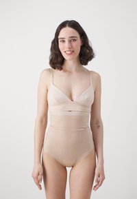 Naakt bodysuit met een V-halslijn, dunne verstelbare bandjes en een hoog-gewijzigd ontwerp; gemaakt van gladde, rekbare stof met een subtiele glans.