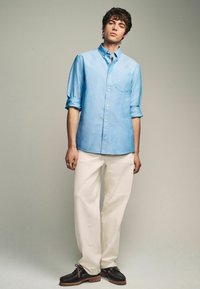 Helle blaue Button-Up-Hemden mit hochgerollten Ärmeln, weiße Hosen und schwarze Schnürschuhe mit braunen Sohlen. Einfaches Design, Baumwollmaterial.