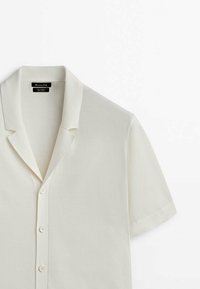 Polo en maille blanche à manches courtes avec col et trois boutons blancs sur le devant, présenté sur un fond blanc.