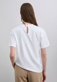 Weißes Baumwoll-T-Shirt mit rundem Ausschnitt und kleinem Schlitzdetail am Rücken, kurzen Ärmeln und abgerundetem Saum.
