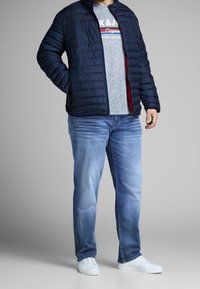 Padded navy jacket with a zippered front, gray T-shirt featuring red and blue stripes, light blue jeans, and white sneakers.