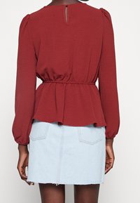 Bordeauxfarvet peplum-top med lange, puffede ærmer; tekstureret stof og detalje med nøglehul på ryggen. Kombineret med en lyseblå denim nederdel.