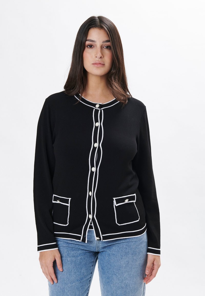 Cárdigan negro con ribete blanco, con cuello redondo, cierres de botones y dos bolsillos frontales. Fabricado en suave tejido de punto.