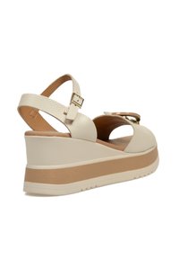 Sandalias de cuña beiges con parte superior de cuero texturizado, que incluyen una correa ajustable, herrajes de hebilla y una plantilla de contraste en tono marrón.