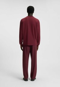 Bordeaux tweedelig outfit met een top met lange mouwen en losse broek, gemaakt van een gladde, zachte stof met een relaxte silhouet.