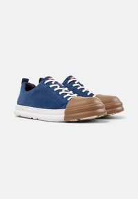 Zapatillas de deporte azul marino con cordones blancos y una tapa de goma marrón en la punta, que muestran un diseño elegante sobre un fondo blanco liso.