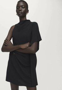 Zwarte jurk met asymmetrisch ontwerp, korte mouwen en gedrapeerd detail op de rok. Gemaakt van een gestructureerde stof, met subtiele hardware-accenten.