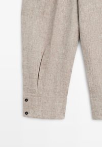 Beige linnenbroek met knoopmanchetten en plooien, met details van de textuur en stof op het onderbeen.