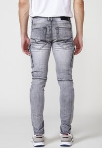 Strakke grijze spijkerbroek van denim met een vervaagde afwerking, voorzien van twee achterzakken en cargozakken aan de zijkanten. Gestikte details bij de naden.