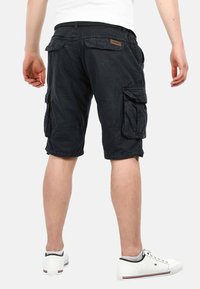Black cargo shorts made of soft fabric, featuring multiple side pockets, a slightly relaxed fit, and a waistband with a logo patch.
