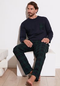 Herres pyjamasæt med en marineblå langærmet overdel med lomme og bukser i grønternet mønster. Stofbeskrivelsen antyder, at det er blødt med en afslappet pasform.