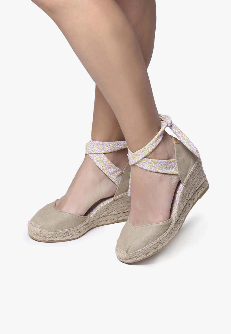 Béžové espadrilové wedgie s kvetinovými potlačami na remienkoch. Textilný zvršok a pletená jutová podrážka. Nízky opätok a dizajn s okrúhlou špičkou, ľahká textúra.