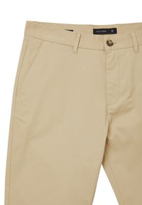 Pantaloni in cotone beige con un design elegante, caratterizzati da tasche anteriori, chiusura con bottone e dettagli di cucitura discreti. Etichetta della marca visibile.