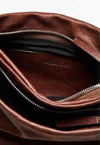 Brown leather bag interior showing a zippered compartment and a logo embossed on the lining. Black fabric accents visible.