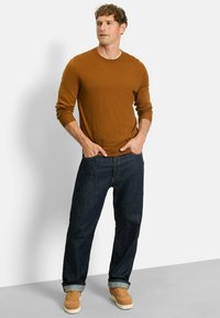 Brauner, langärmeliger Pullover kombiniert mit dunkelblauen Jeans und beigen Sneakers. Der Pullover hat gerippte Bündchen und ein klassisches Rundhalsdesign.