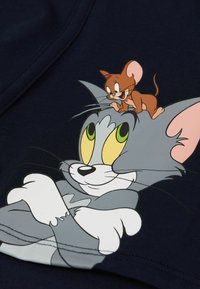 Tejido de algodón de color azul marino que presenta un gráfico de dibujos animados de un gato gris con ojos amarillos y un ratón marrón en la cabeza, detallado con acentos blancos.