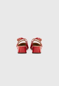 Rote Lackleder-Sandalen mit Blockabsatz, verstellbarem Knöchelriemen und mehreren Riemen an den Seiten. Glatte Textur, minimalistisches Design.