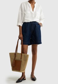 Blusa bianca morbida e ampia; pantaloni shorts in denim scuro; ballerine nere; borsa intrecciata con dettagli in pelle beige e nappina.