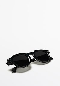 Sonnenbrille mit einem glänzenden schwarzen Kunststoffrahmen, übergroßen rechteckigen Gläsern und einem geometrischen Design. Verfügt über dezente Logoakzente an den Bügeln.