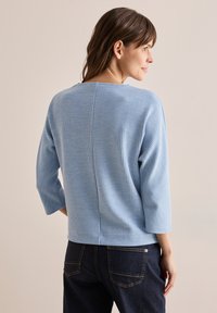 Ljust blå ribbad tröja med rund halsringning och trekvartslånga ärmar, som är ihop med mörk denim jeans. Subtil vertikal randig mönster.