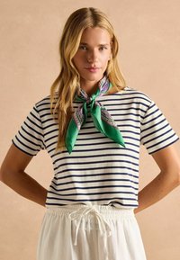 Raiutud puuvillane T-särk valge ja tumesinise lööbiga, sobitatud rohelise ja mustrilise siidist salliga. Omab lühikesi varrukaid ja lõdvemat lõike.