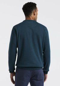 Donkerblauwe crewneck sweatshirt van textiel met een gestructureerde stof, ribbelmanchetten en onderrand. Eenvoudig ontwerp, achteraanzicht, gedragen met donkere broeken.