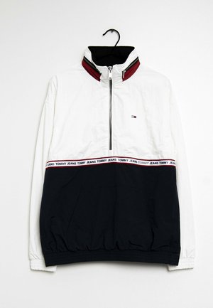 Wiatrówka z półzamkiem, biała góra, granatowy dół, kołnierz z czerwonym obszyciem, elastyczne mankiety oraz logo "Tommy Jeans" na środkowej części.