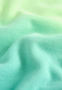 Tessuto verde chiaro con una superficie liscia, che mostra sfumature sottili da verde chiaro a verde scuro. Tricot finemente con un motivo di cucitura visibile.