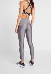 Leggings deportivos grises con una textura suave y detalles de crisscross en los laterales, combinados con un sujetador deportivo negro con tirantes que presenta acentos de logotipo.
