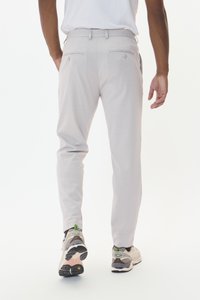 Pantalons gris clair avec une coupe slim, dotés de deux poches arrières et d'une texture lisse. Portés avec des baskets beiges et grises.
