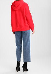 Sudadera roja con capucha de corte holgado, combinada con vaqueros azules recortados y botines negros con tacón. Diseño simple, detalles mínimos.