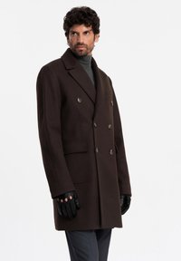 Double-breasted dark brown wool coat with peak lapels, two front pockets, and decorative buttons, paired with black fingerless gloves.